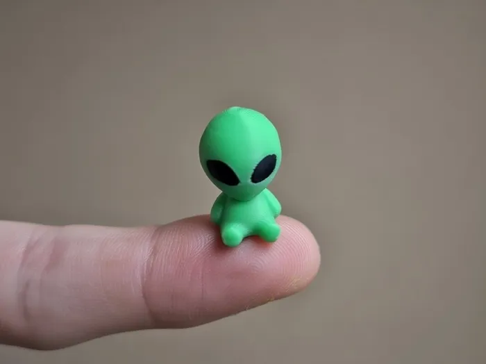 A tiny green printed alien on a fingertip.