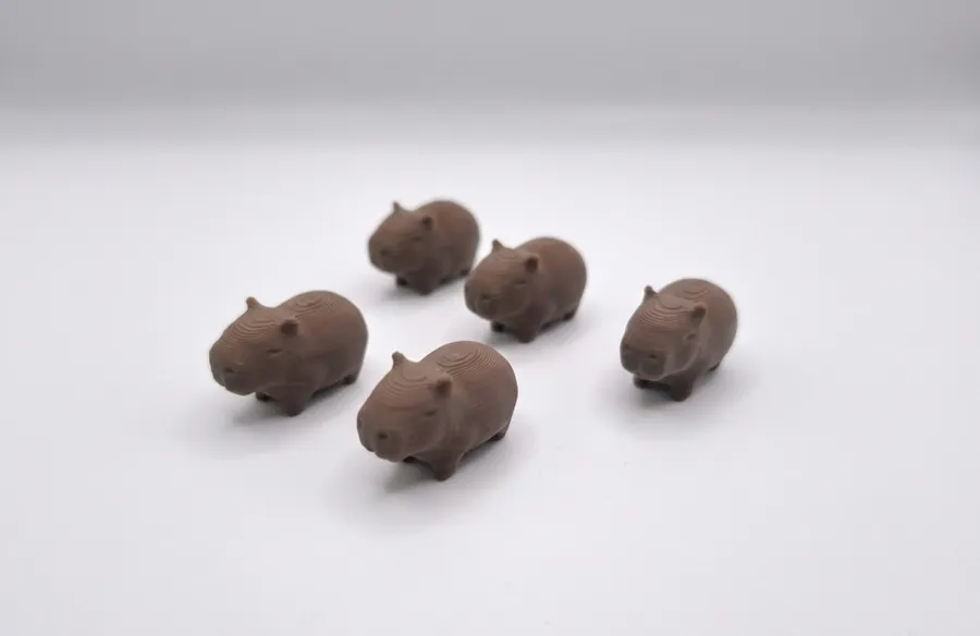 Five tiny printed capybaras on a white table.