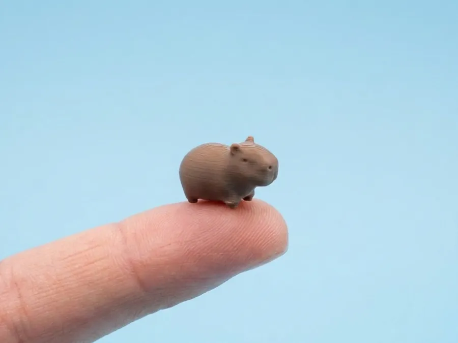 A tiny printed capybara standing on a fingertip.